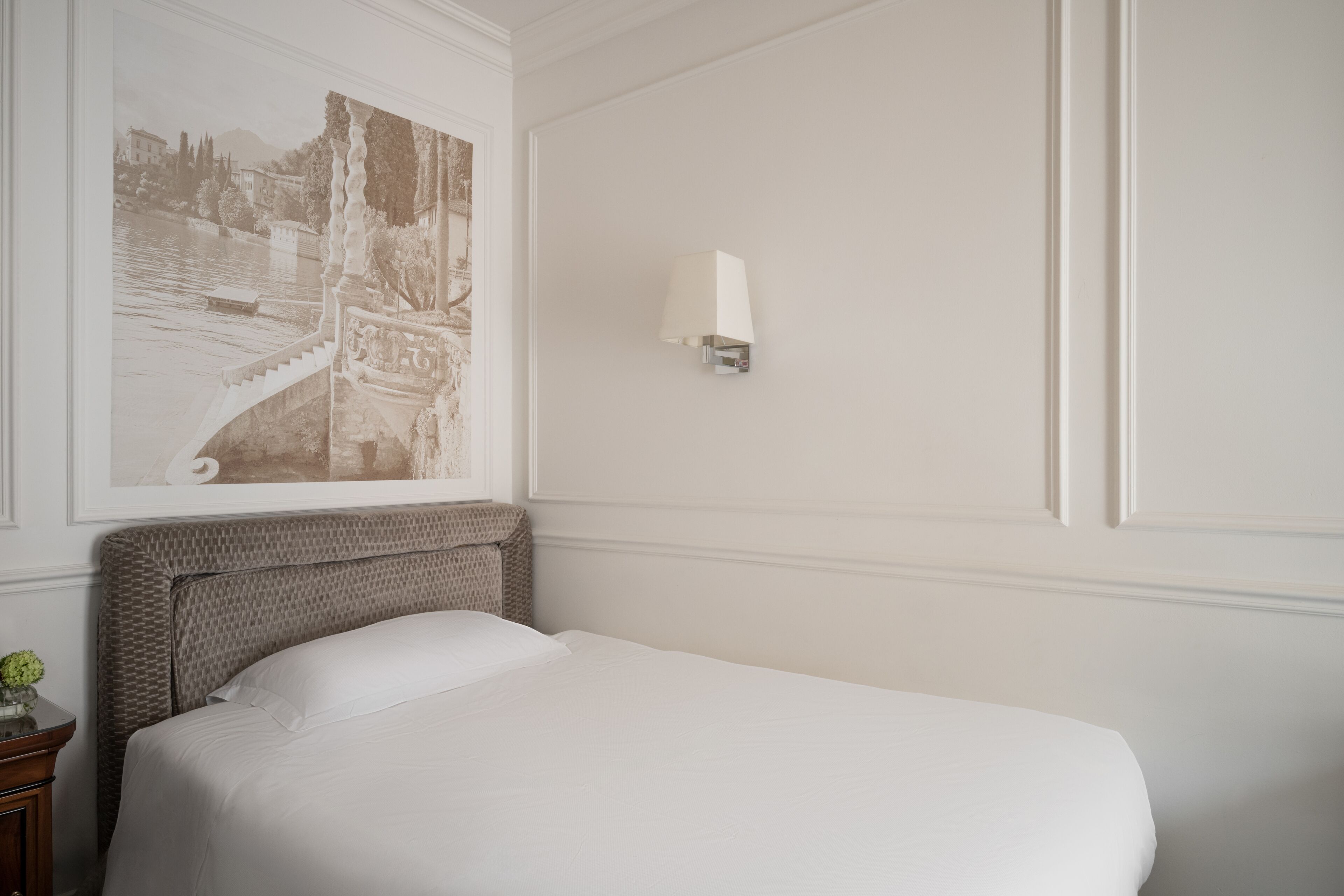 Un letto rifatto con cura in una stanza con un quadro incorniciato appeso al muro e una lampada fissata alla parete.