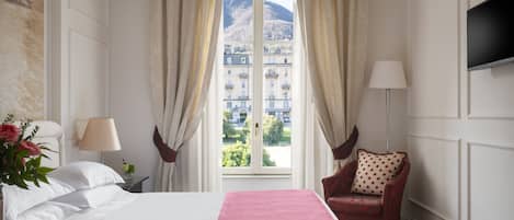 Una habitación de hotel con cama, una silla, televisor y ventana con cortinas.