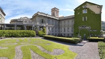A building with a formal entrance, a landscaped garden with a winding path, and a sign for 'BAR DELLE TERME'.