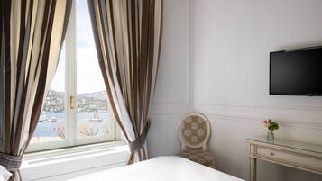 Una habitación de hotel con cama, una silla, un escritorio, televisión y ventana con cortinas.