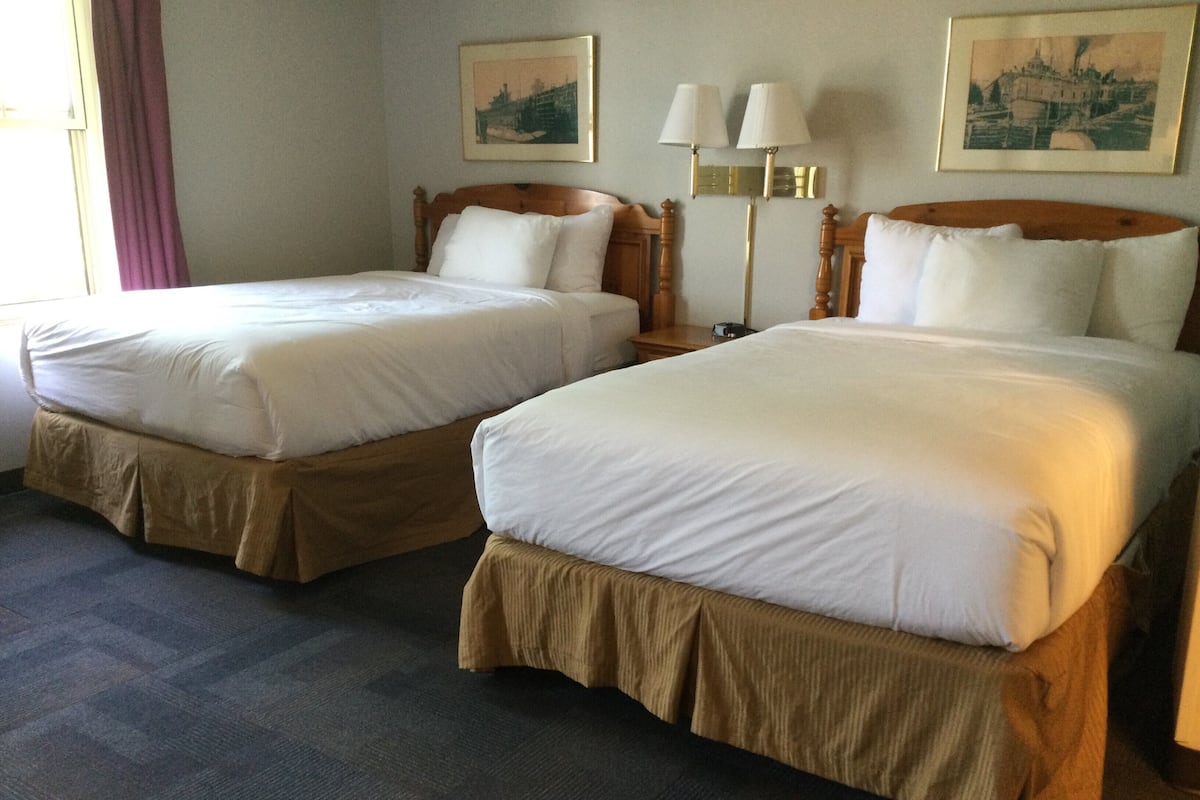 Two single beds with wooden headboards and matching headboards, a nightstand with a lamp, and two framed pictures on the wall.