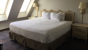 A neatly made bed in a room with two bedside tables, each with a lamp. The room has a sloped ceiling with skylights. - The Hotel Ojibway, Trademark Collection by Wyndham (Sault Ste. Marie)