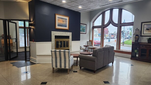A lobby with a fireplace, seating area, and large windows offering a view of the street. - The Hotel Ojibway, Trademark Collection by Wyndham (Sault Ste. Marie)
