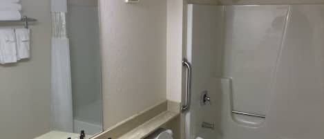 A bathroom with a sink, mirror, toiletries, a toilet, and a shower.