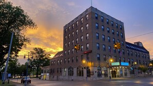 A multi-story building with a prominent American flag on top, featuring a large entrance with a sign that reads "JIBWAY." - The Hotel Ojibway, Trademark Collection by Wyndham (Sault Ste. Marie)