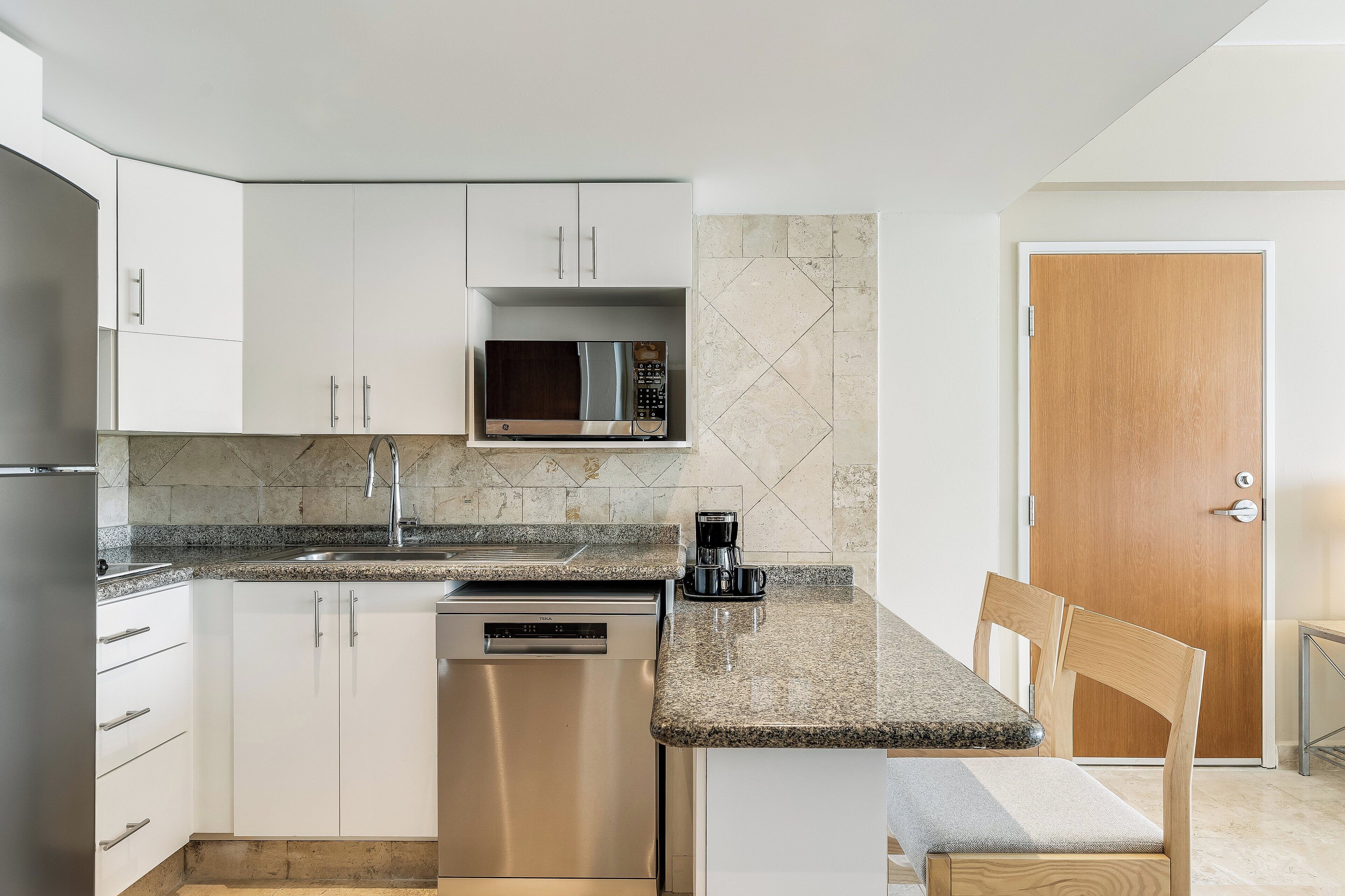 Una cocina compacta con armarios blancos, microondas integrado, cafetera y lavavajillas.