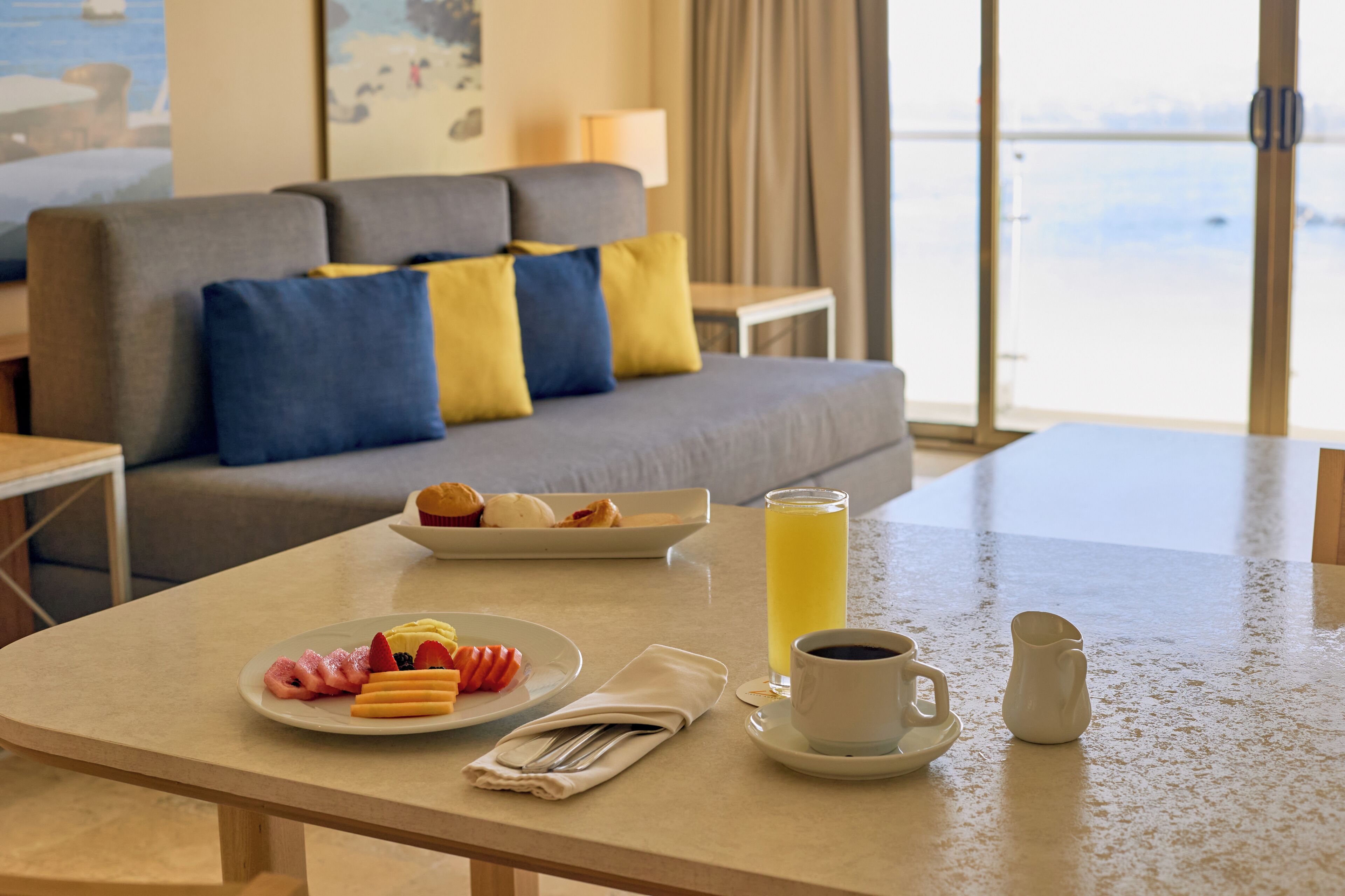 A dining area with a table set for breakfast, a sofa with cushions, and a view of the beach.