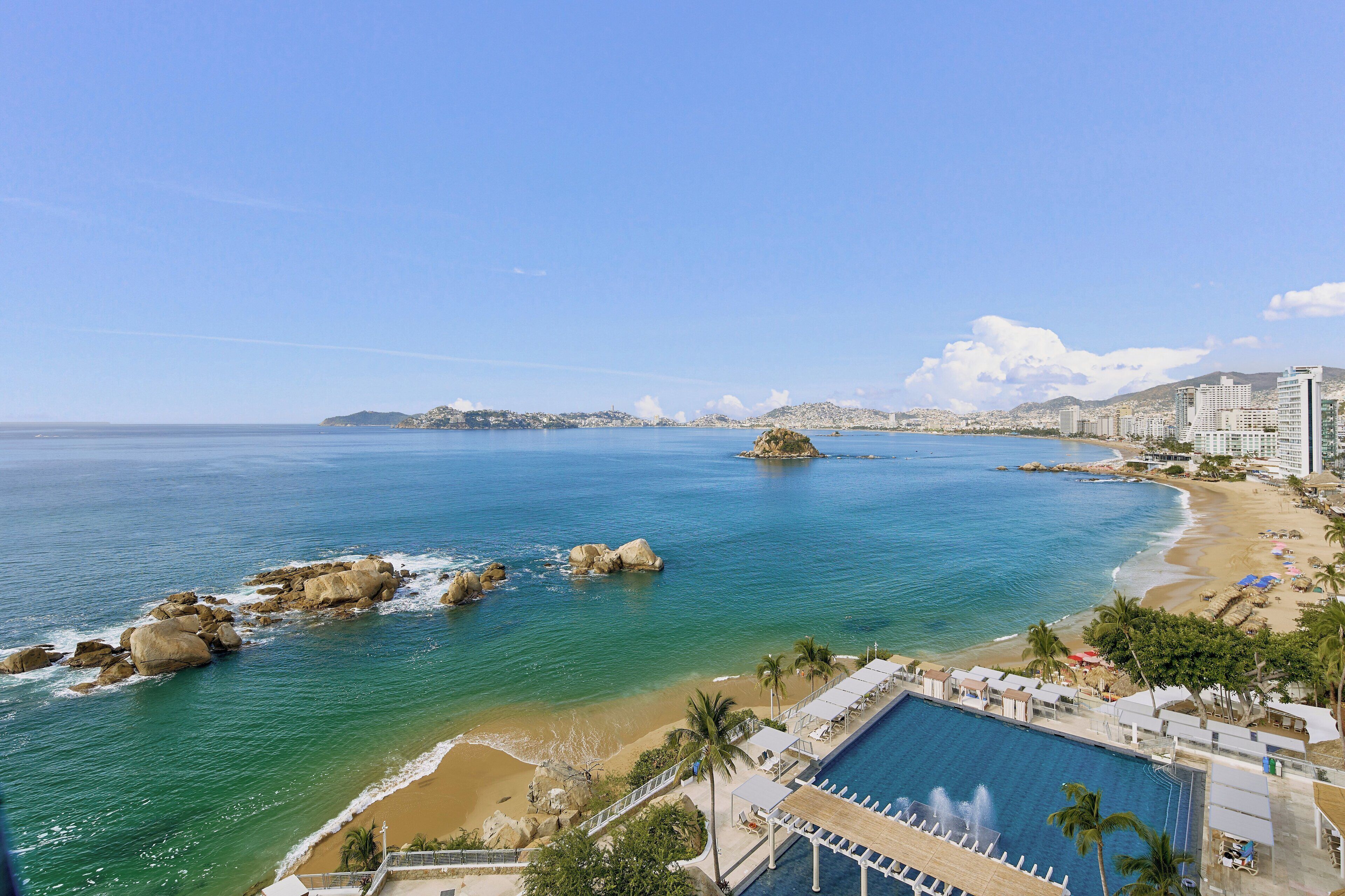 A coastal hotel with a pool, beach, and rocky outcrops.
