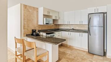 A modern kitchen with white cabinets, a stainless steel refrigerator, a microwave, and a granite countertop.