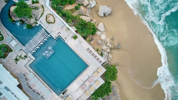 Vista aérea de un complejo turístico con piscina, playa y costa rocosa.