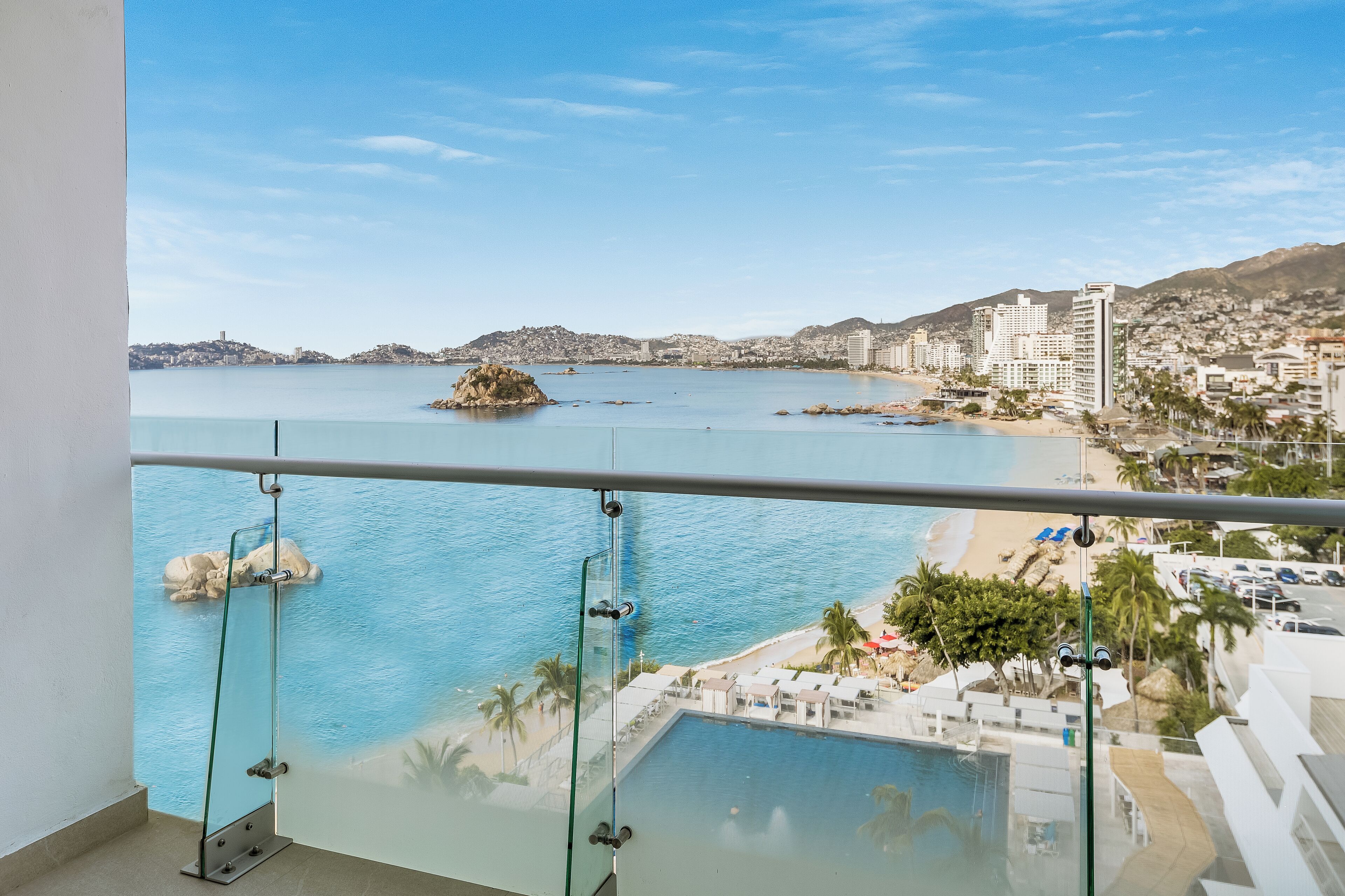 Een balkon met een helder uitzicht op een strand, een zwembad en een stadsgezicht op de achtergrond.