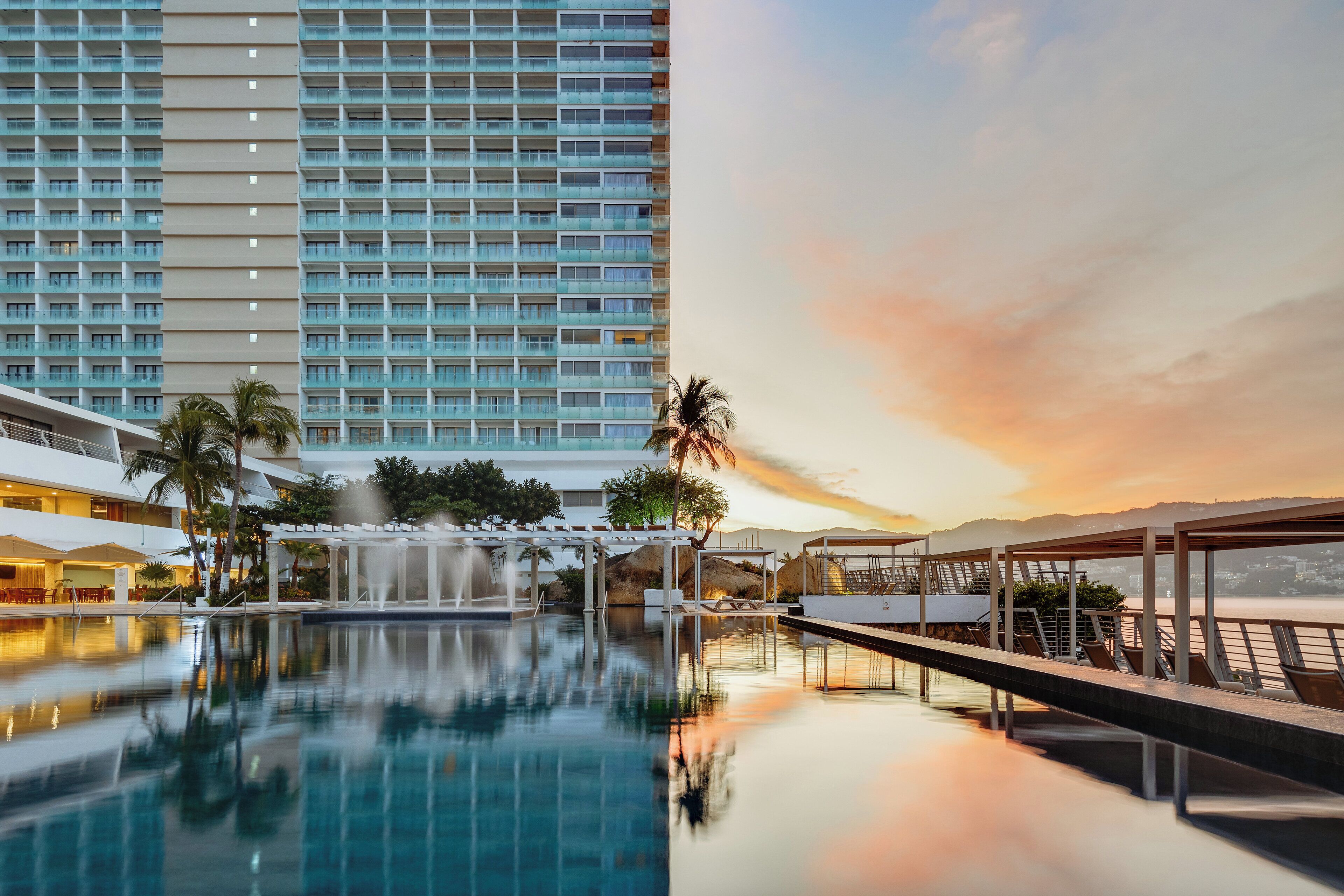 A hotel with a large building, a pool, and a sunset view.