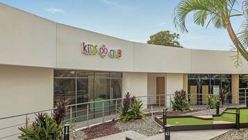A building with a sign reading "Kids Club" and a landscaped outdoor area with plants and a palm tree.