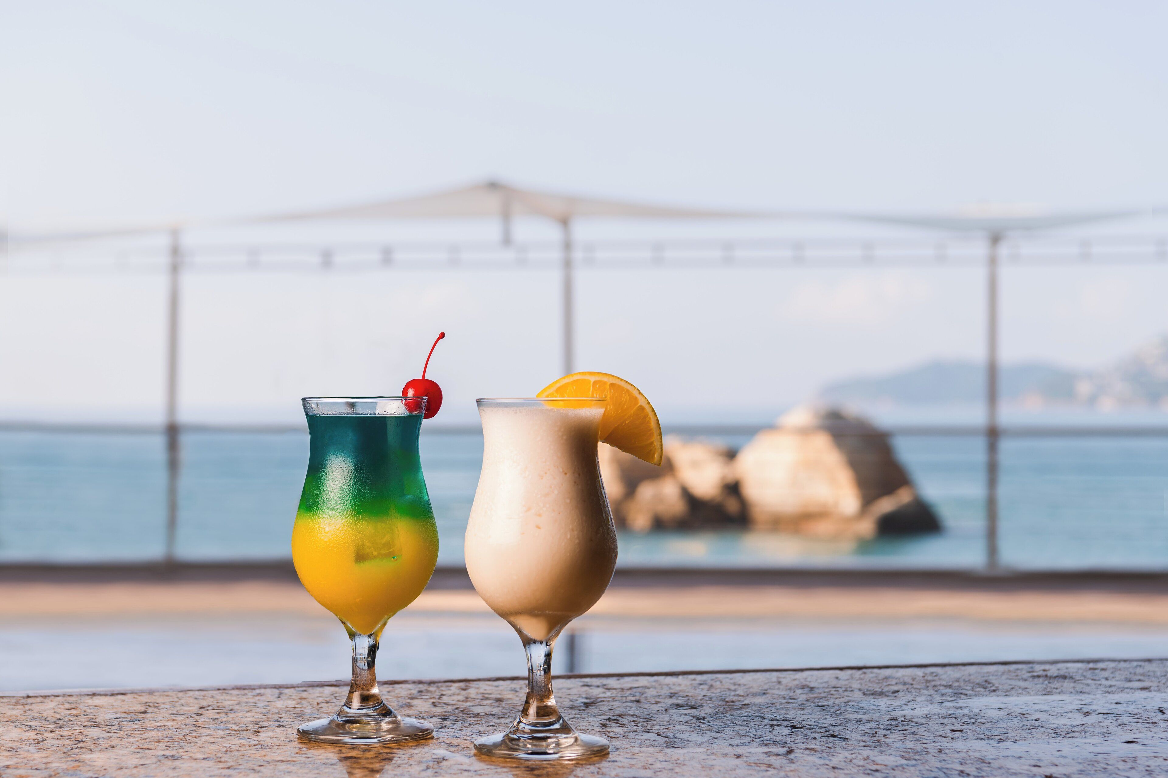 Deux cocktails sur une table, avec vue sur la mer et un pont en arrière-plan.