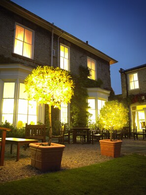 A building with large windows, a patio area with outdoor seating, and two illuminated trees. - Best Western Forest & Vale Hotel (Pickering)