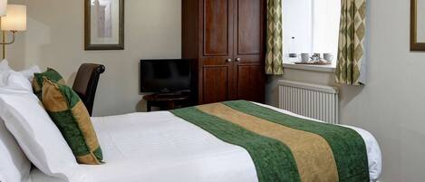 A hotel room with a bed, a television, a wardrobe, a window with curtains, and a radiator.