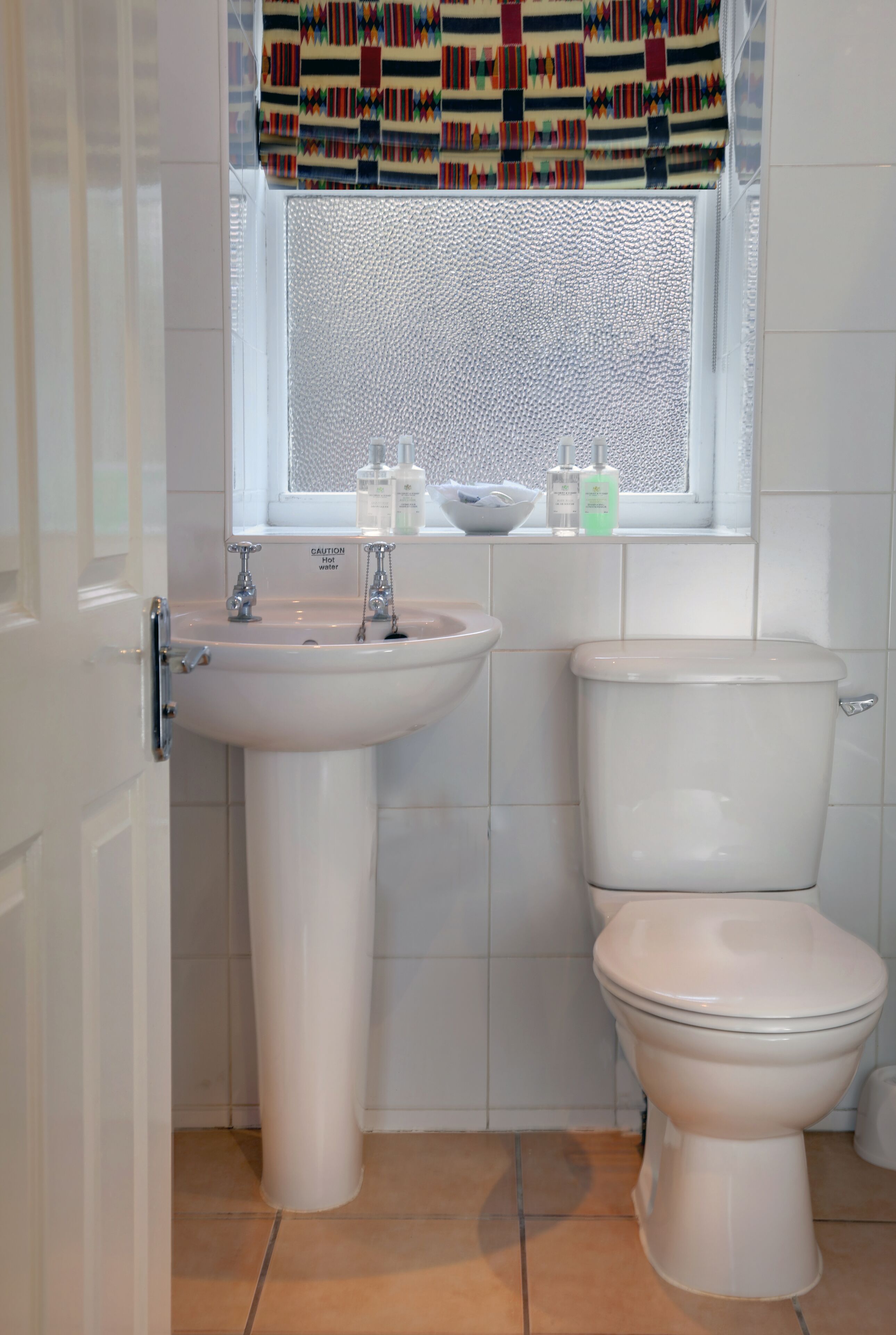 Casa de banho com uma sanita, lavatório branco e janela com cortinas estampadas.
