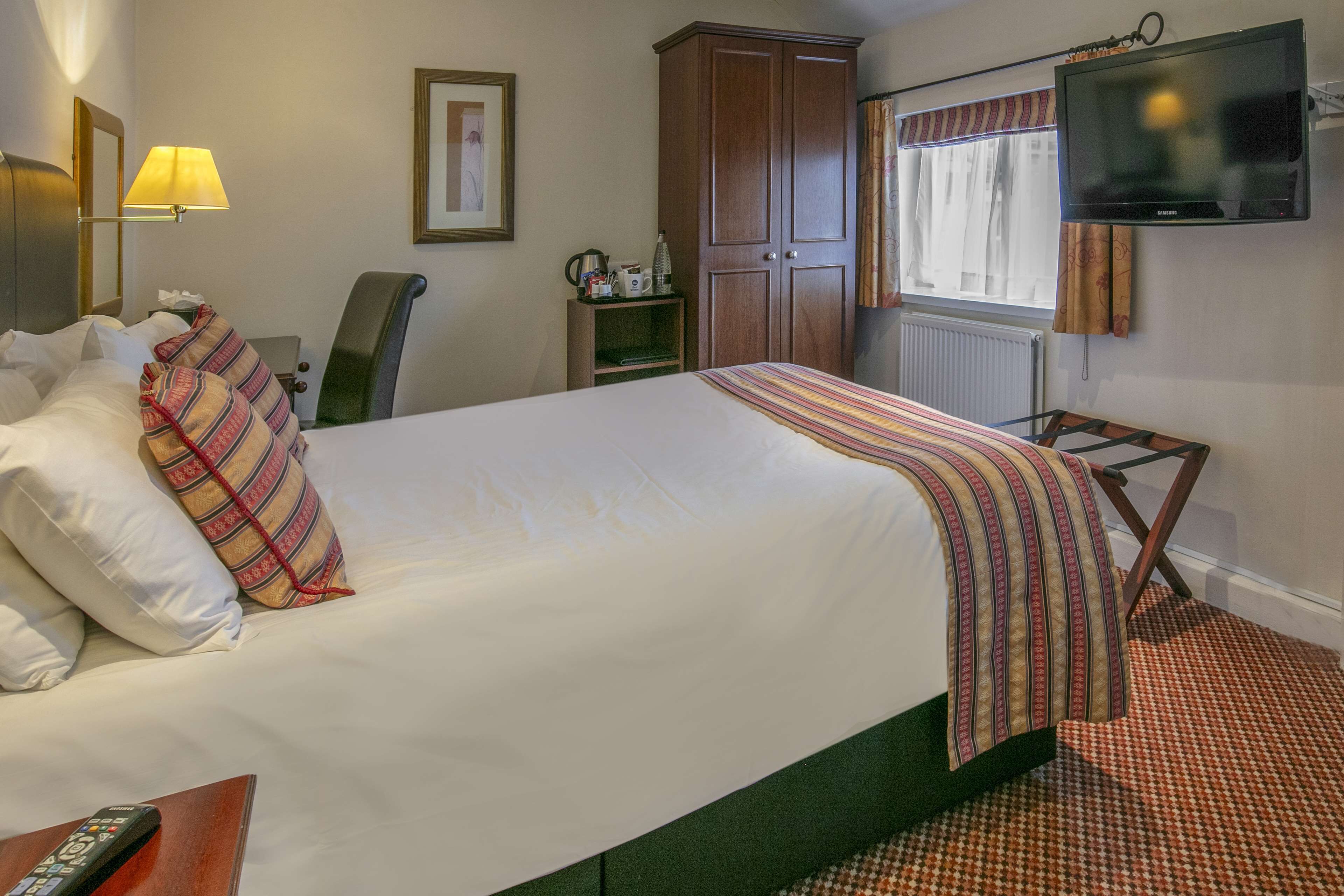 Una habitación de hotel con una cama grande, un escritorio con lámpara, un televisor y un armario.