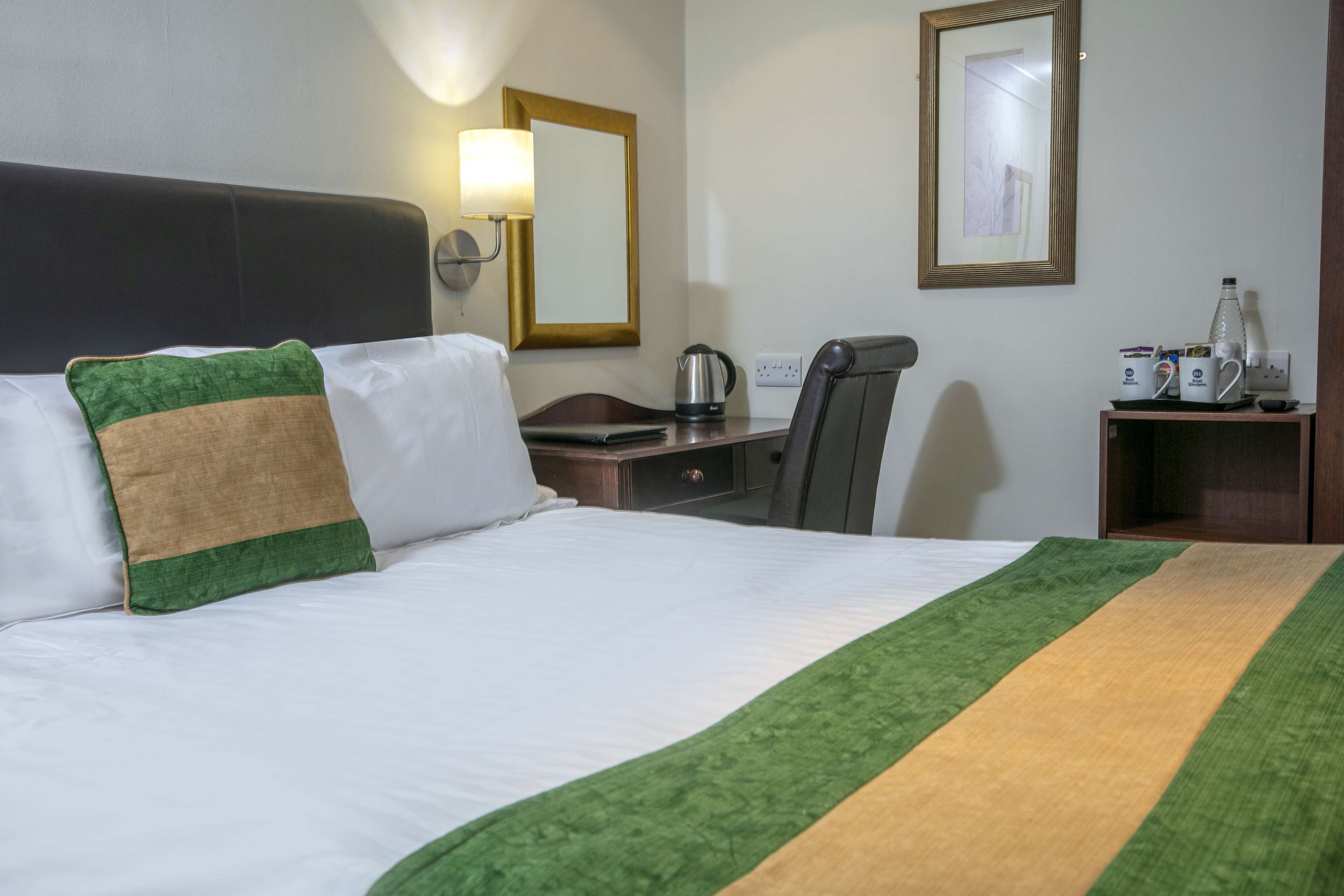 Una habitación de hotel con una cama, un escritorio, una silla, una lámpara y un espejo.