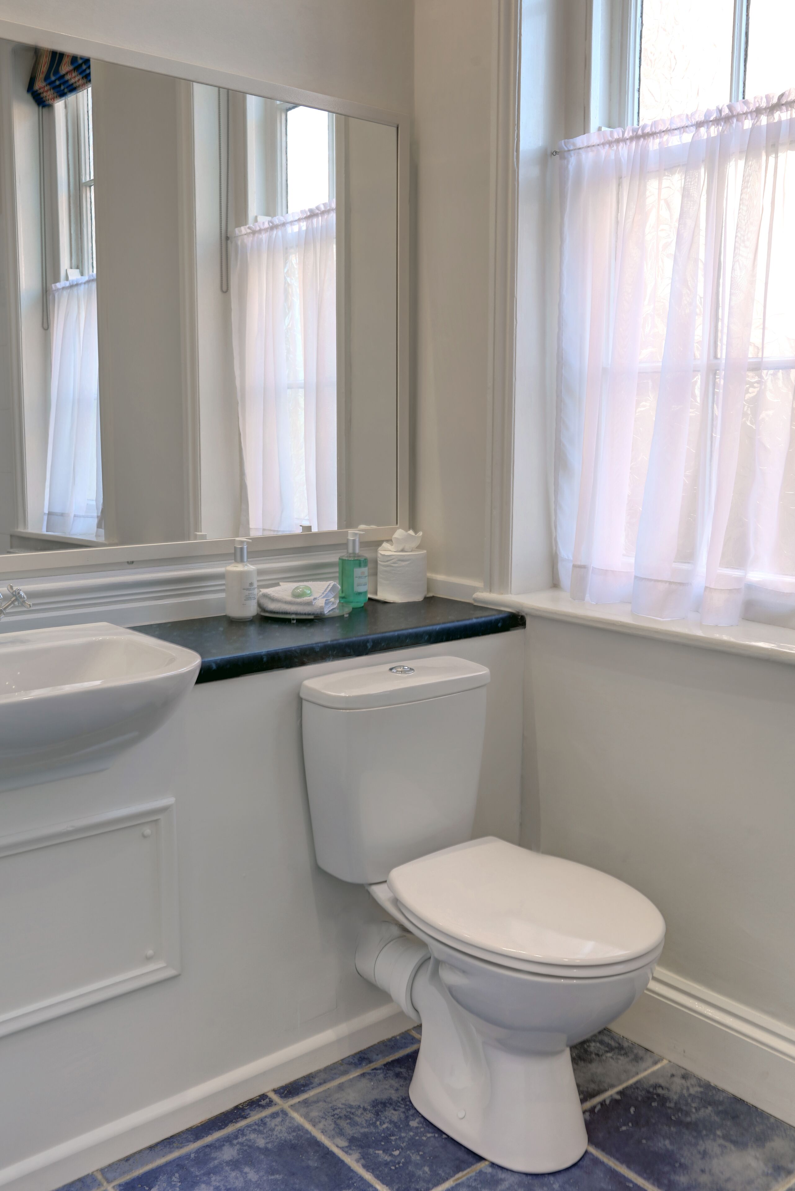 A bathroom with a white sink, toilet, and mirror. There are toiletries on the counter.