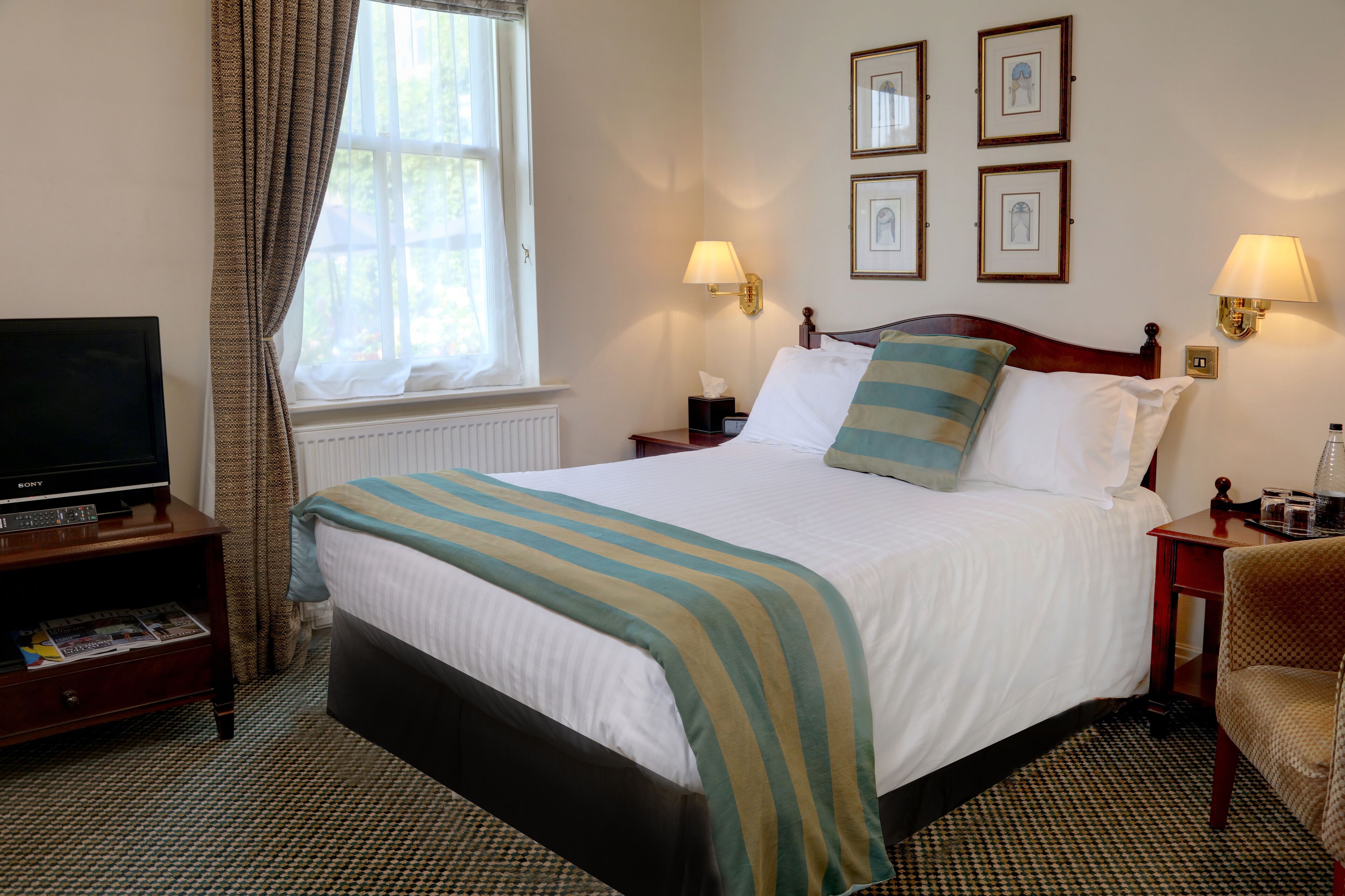 A hotel room with a bed, a television on a stand, a nightstand with a lamp, and a chair.