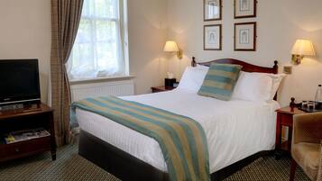 A hotel room with a bed, a television on a stand, a nightstand with a lamp, and a chair.
