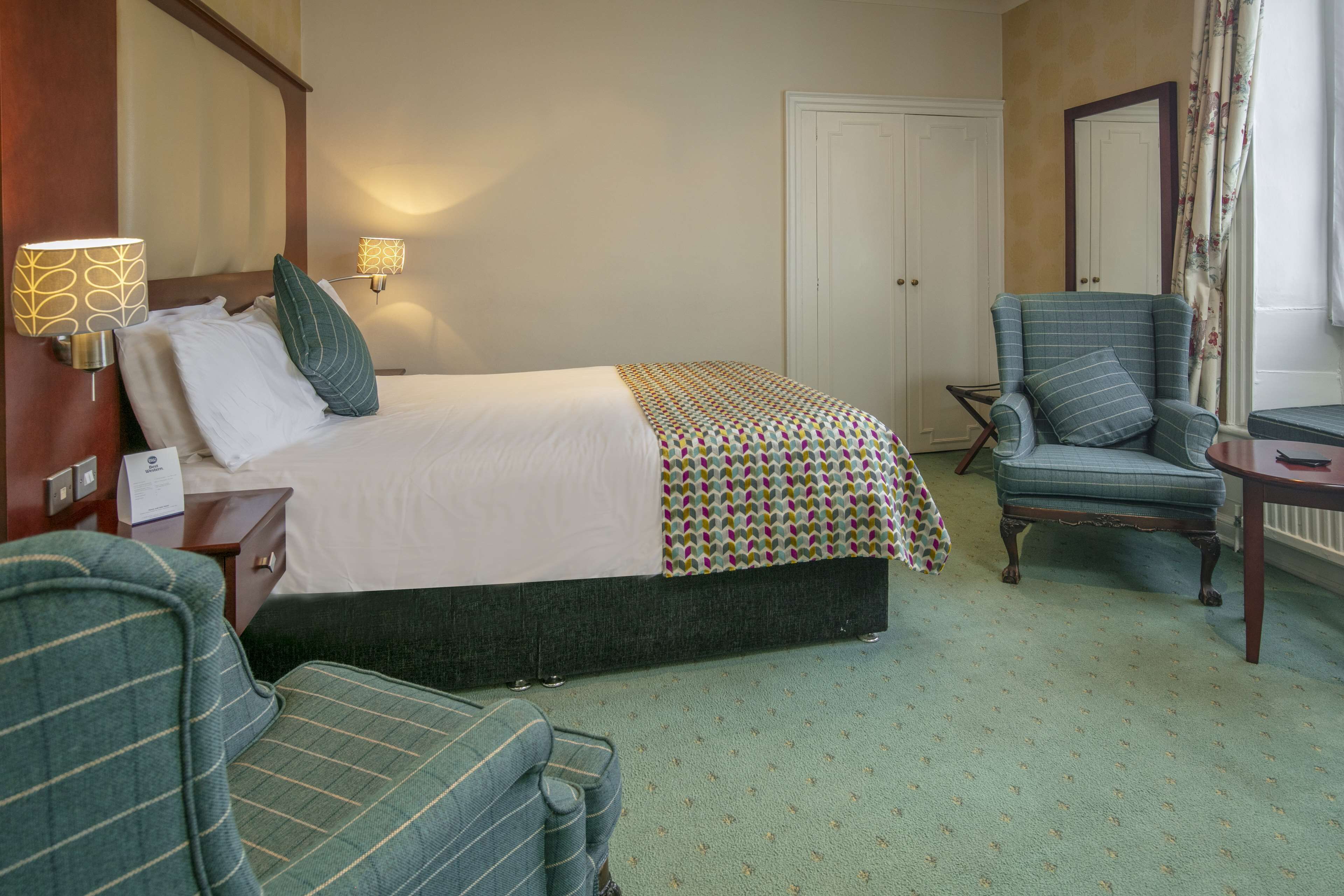 A hotel room with a bed, a chair, a desk, and a wardrobe.