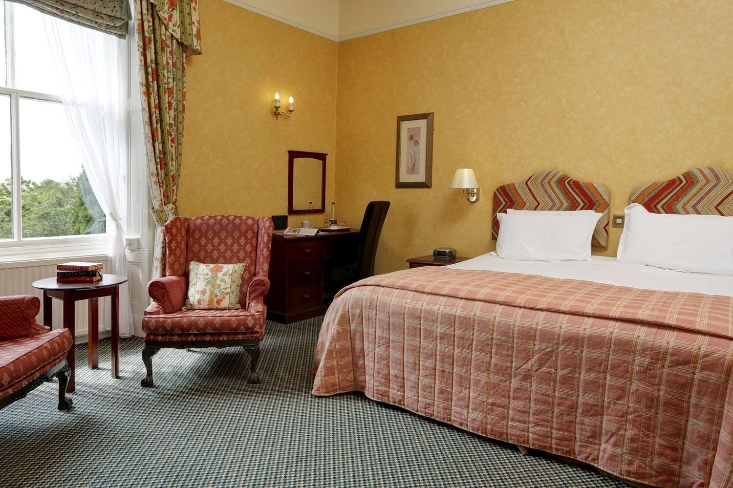 Ein Hotelzimmer mit einem großen Bett, einem Sessel, einem Schreibtisch und einem kleinen Tisch.