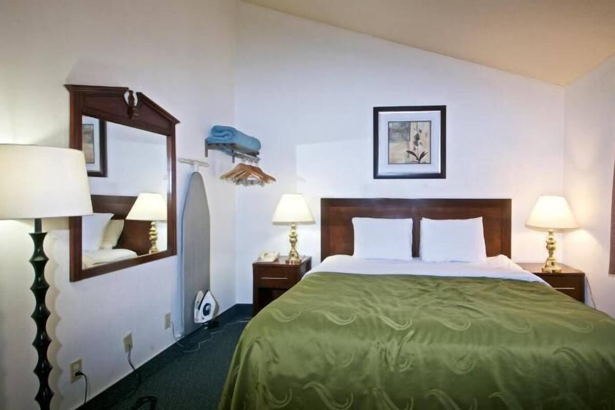 A hotel room with a bed, two bedside tables with lamps, a mirror, a picture on the wall, and a window with curtains.