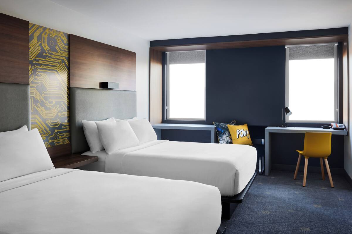 A hotel room with two beds, a desk, a chair, and a large window.