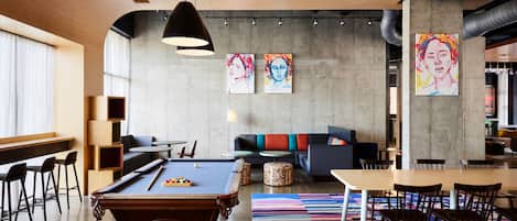 A modern lounge area with a pool table, seating, and artwork on the walls.