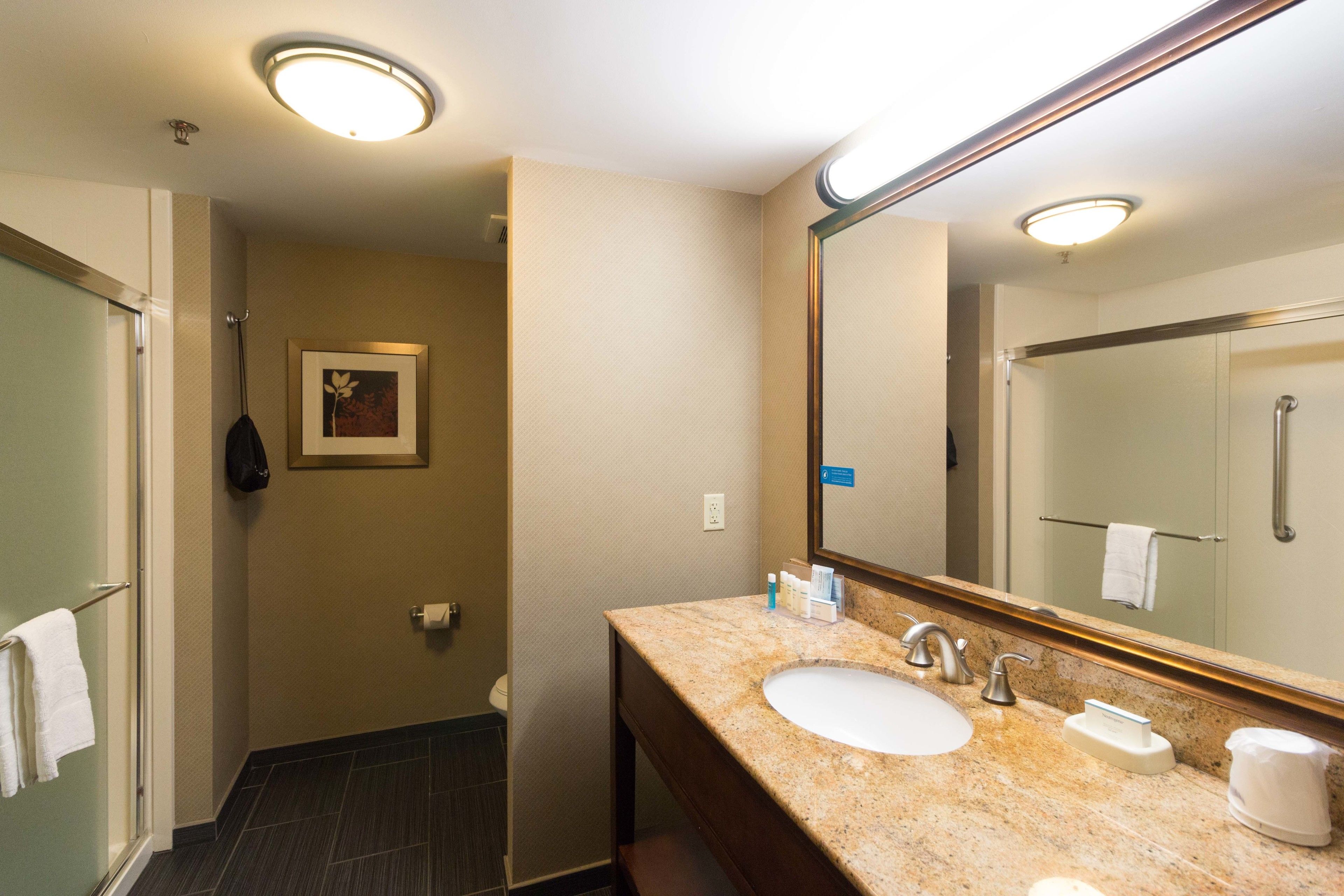 A hotel bathroom with a marble sink, a large mirror, and a shower area.
