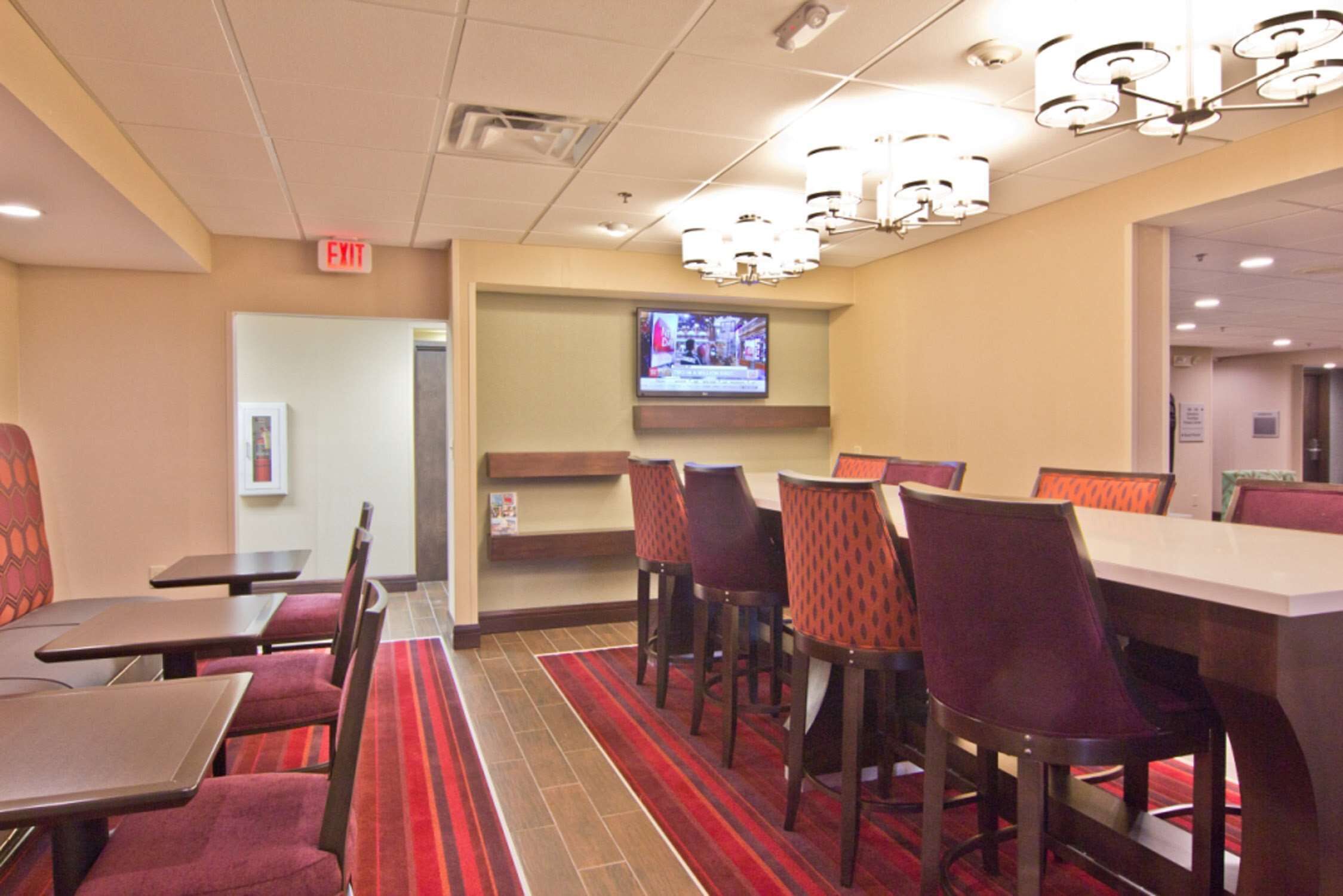 Una zona de dinar d'hotel amb taules i cadires, una pantalla de televisió i una catifa vermella.