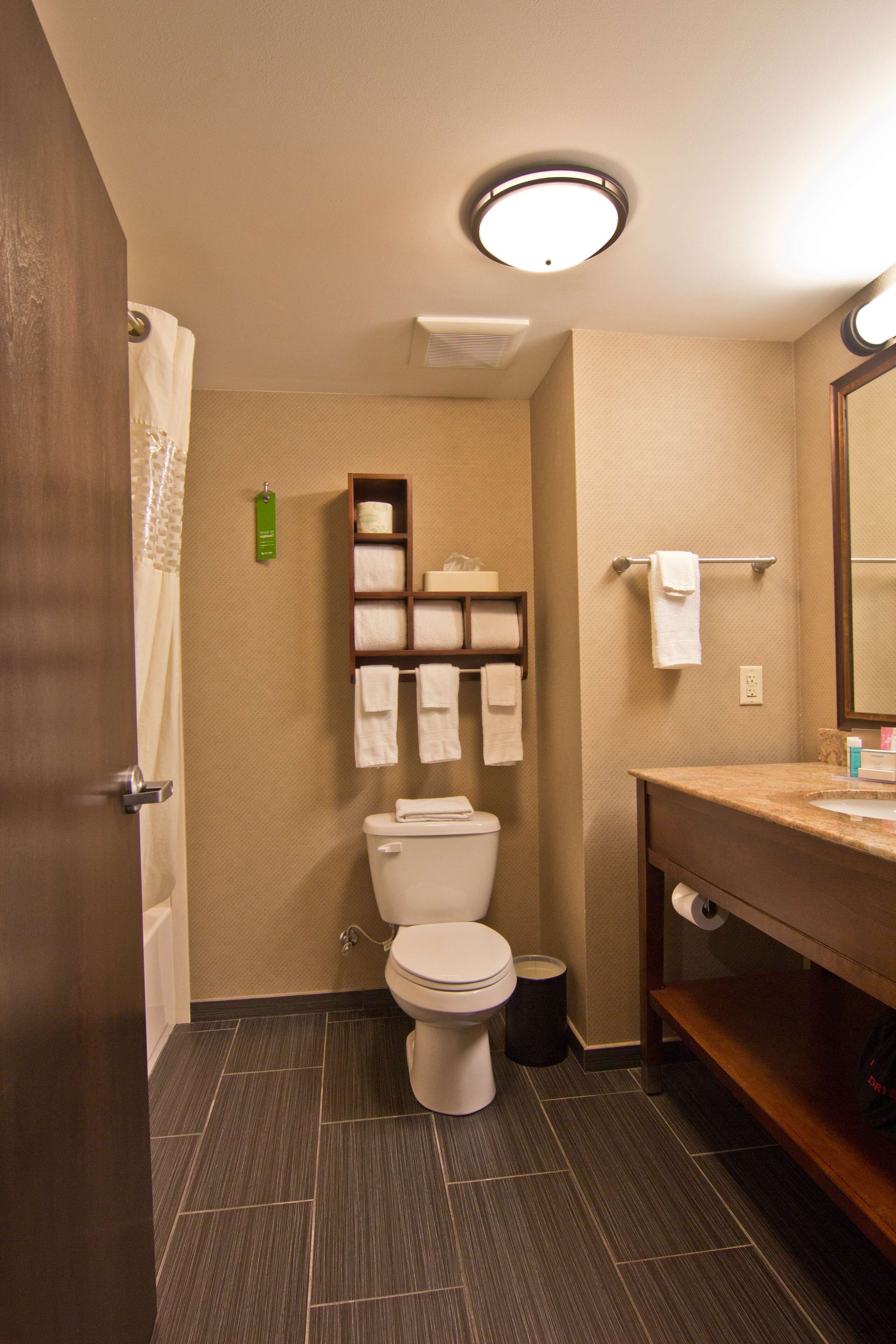 A bathroom with a toilet, a sink, a mirror, and a shelf with towels.