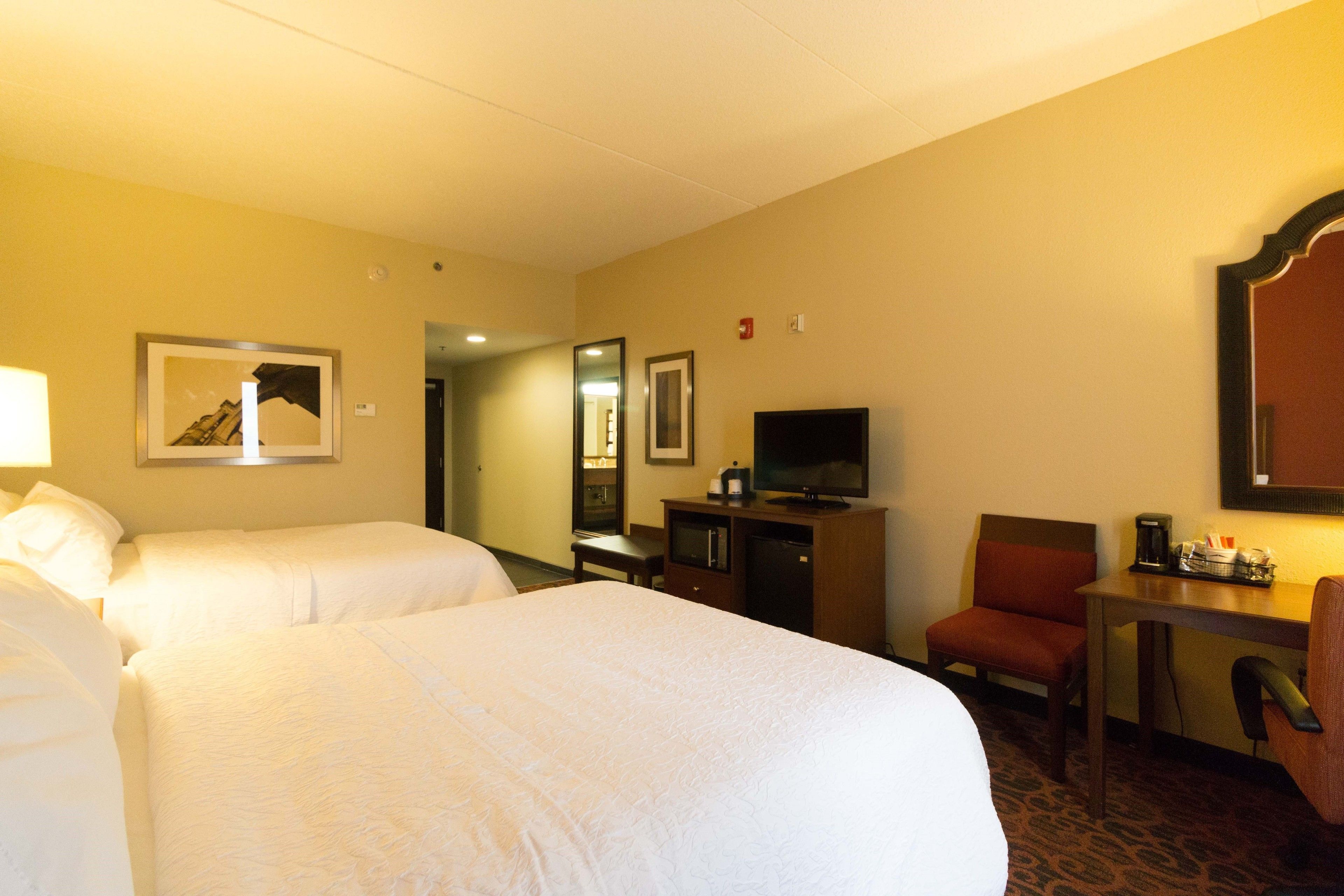 A hotel room with two beds, a desk with a chair, a television, and a coffee maker.