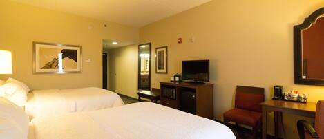 A hotel room with two beds, a desk with a chair, a television, and a coffee maker.