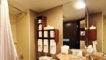 A hotel bathroom with a toilet, sink, and a mirror. There are towels hanging on a rack and a shower curtain.