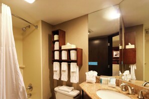 A hotel bathroom with a toilet, sink, and a mirror. There are towels hanging on a rack and a shower curtain.