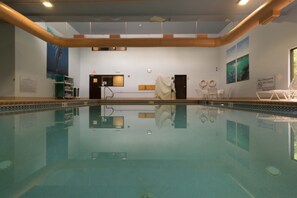 A swimming pool with a tiled floor, a changing room, and a door with a towel hanging on it.