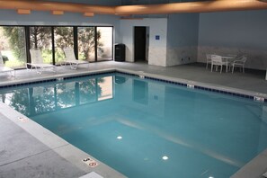 An indoor swimming pool with clear water, lounge chairs, and a seating area with tables.