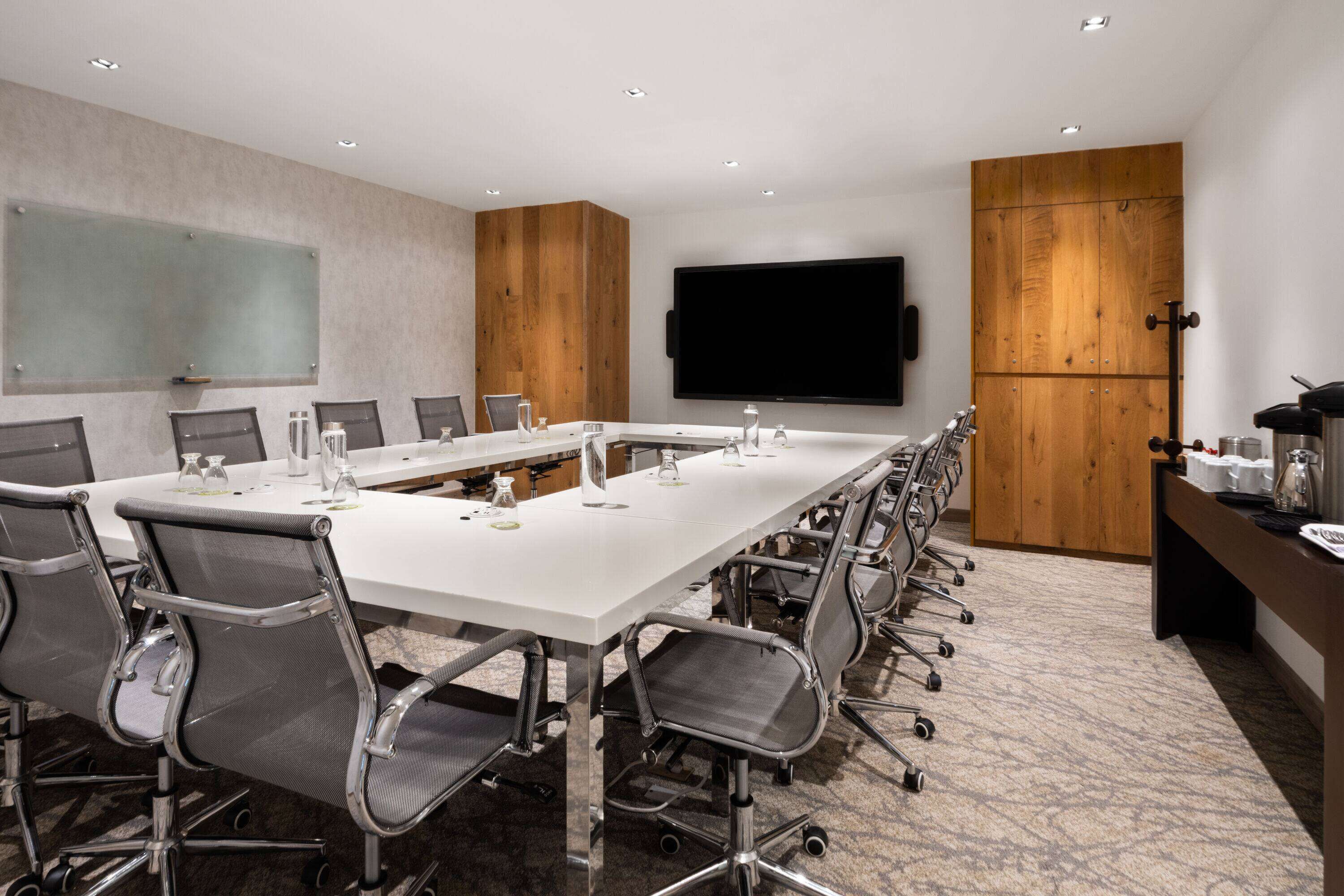 A conference room with a long table, chairs, a TV, and wooden cabinets.