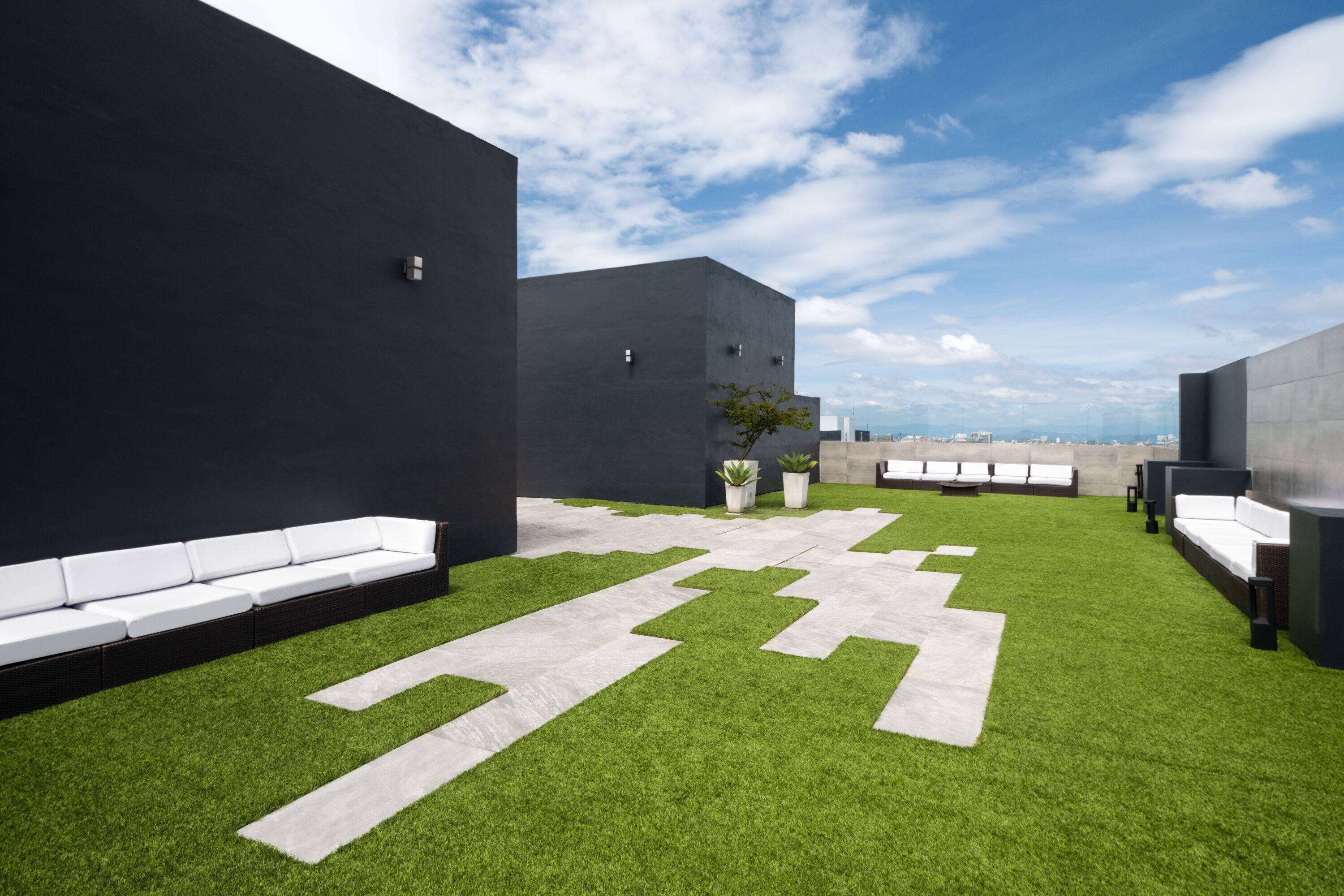 A rooftop terrace with artificial grass, white seating, and a clear sky.