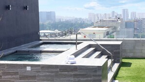 A rooftop pool with a city view, a set of stairs, and a small grassy area.