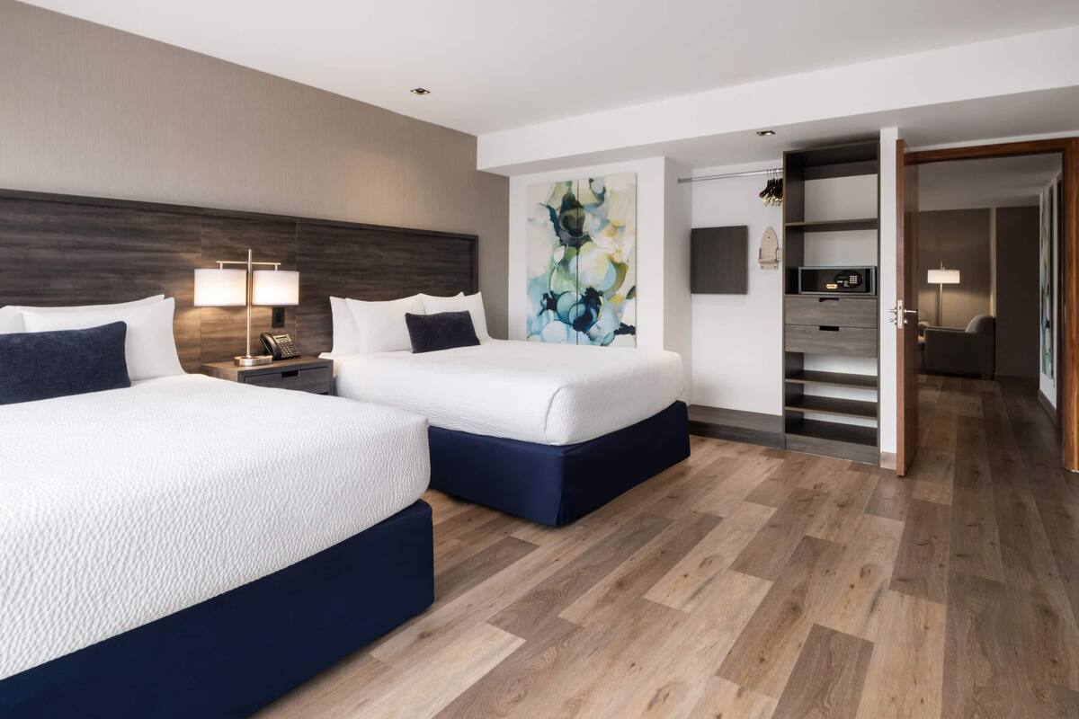 Ein Hotelzimmer mit zwei Betten, Holzboden, einem Bild an der Wand und einem Schreibtisch mit Lampe.