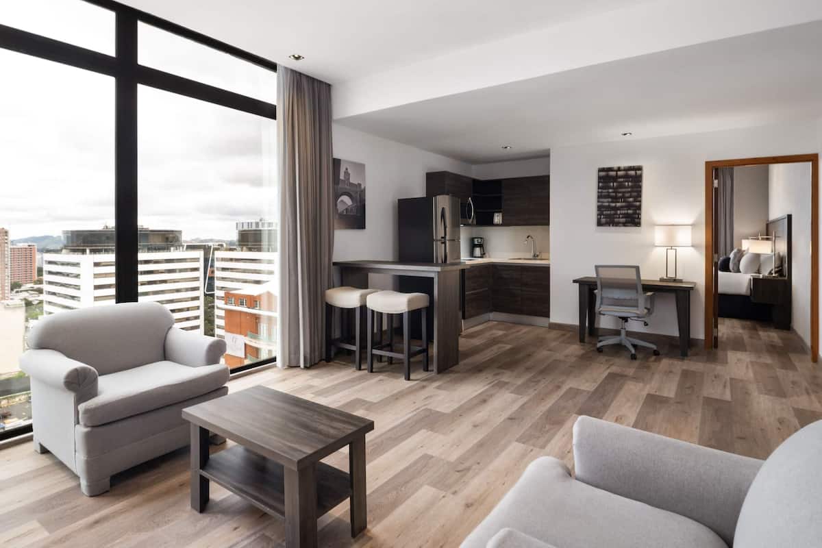 Eine moderne Wohnung mit Küche, Essbereich und Sitzgelegenheiten. Sie bietet große Fenster, Blick auf die Stadt und eine Kombination aus Holz- und Metallelementen.