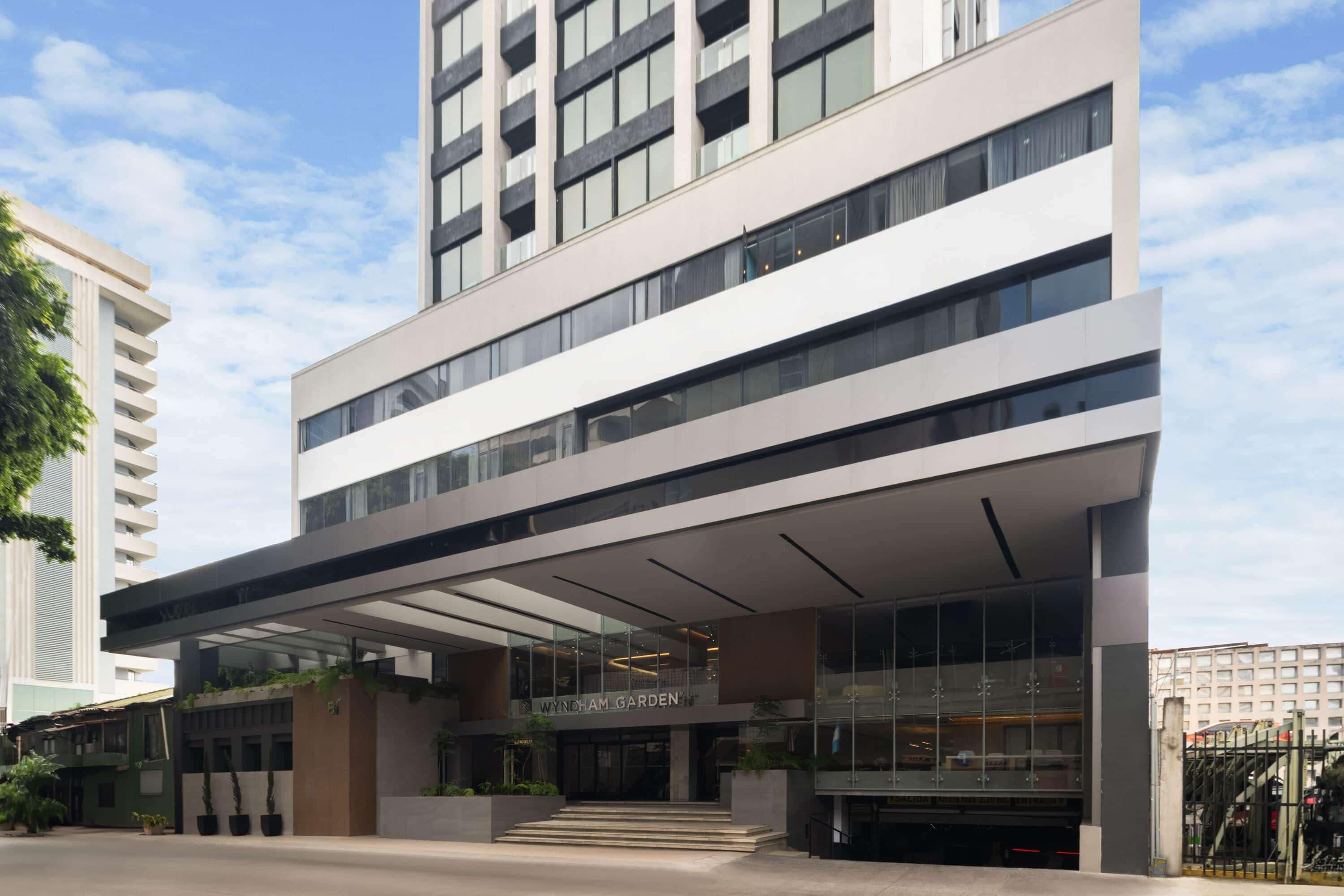 A modern hotel with a prominent entrance, a covered outdoor area, and a name sign.
