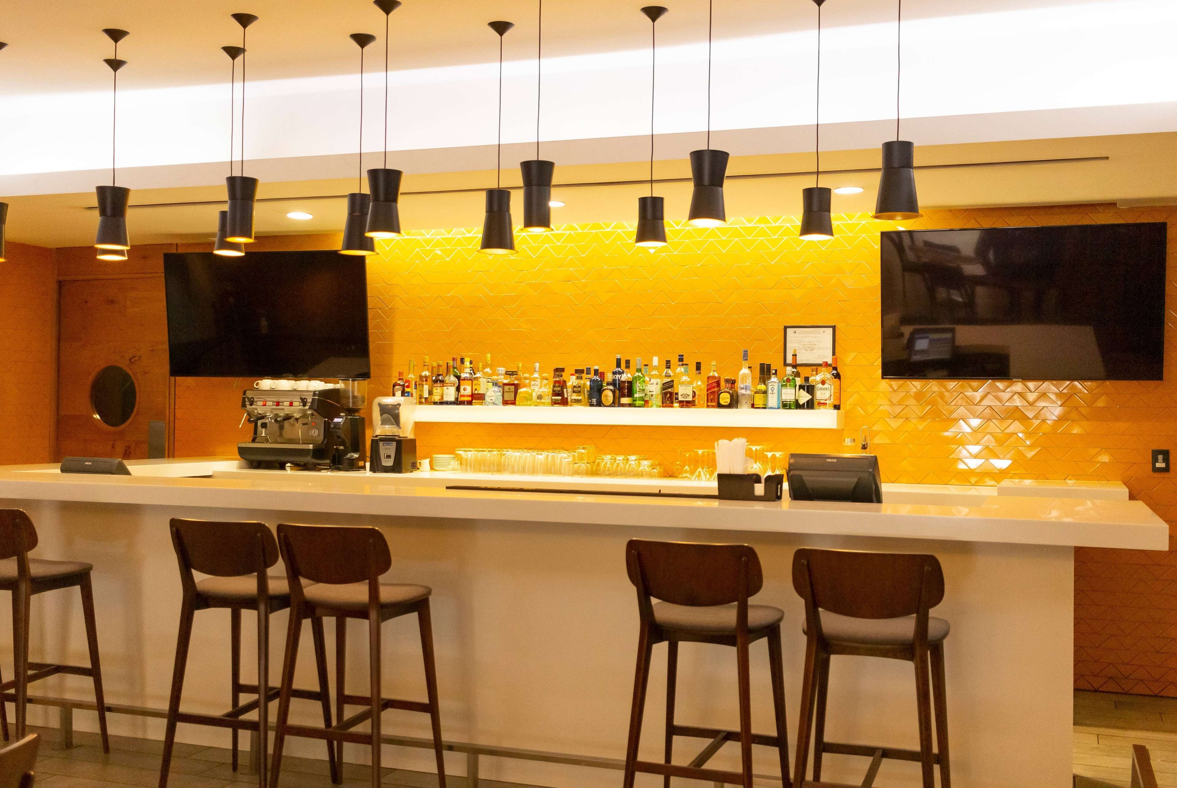 Una zona de bar con una barra alargada, varios taburetes y una gran variedad de botellas y vasos.