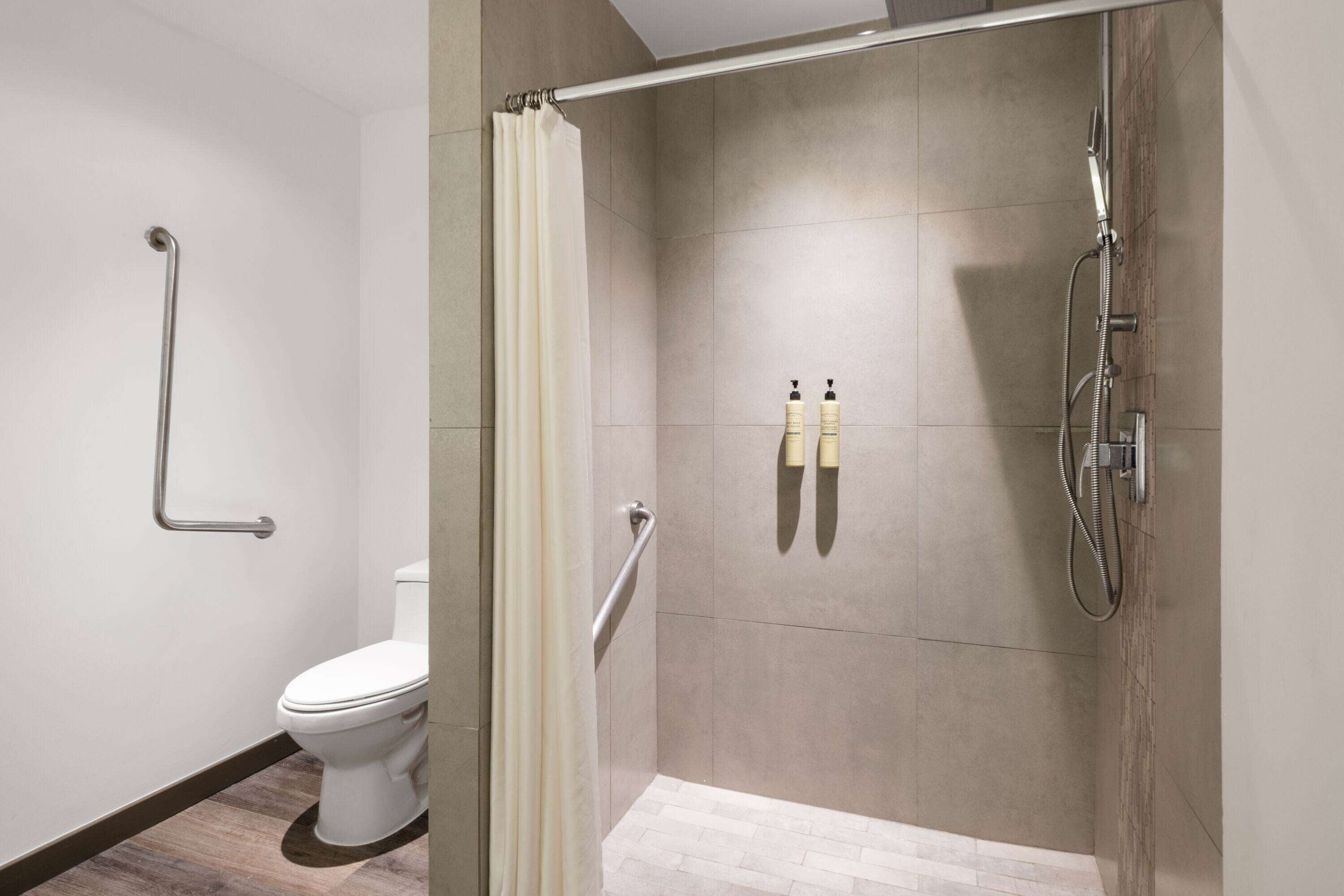 Un baño moderno con ducha, inodoro y barras de apoyo.