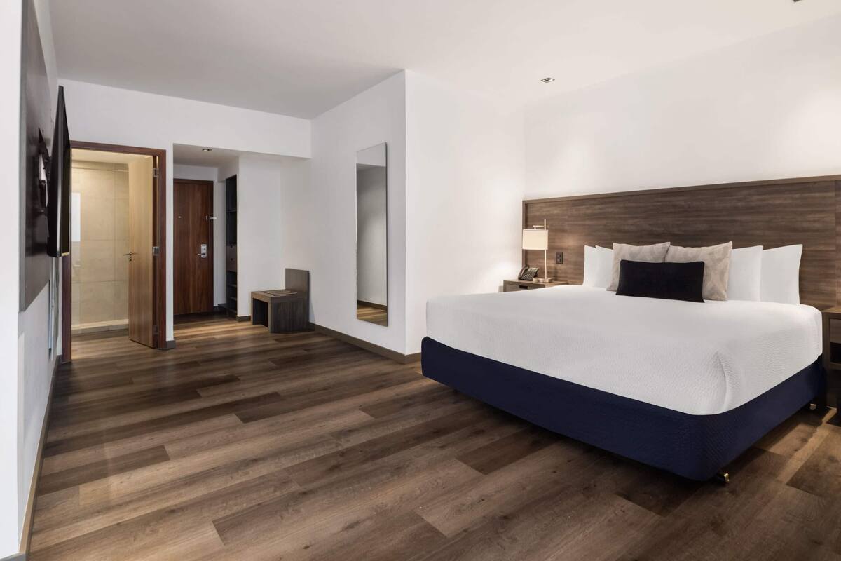 Ein modernes Hotelzimmer mit einem großen Bett, Holzboden, einem Spiegel und einem Nachttisch.