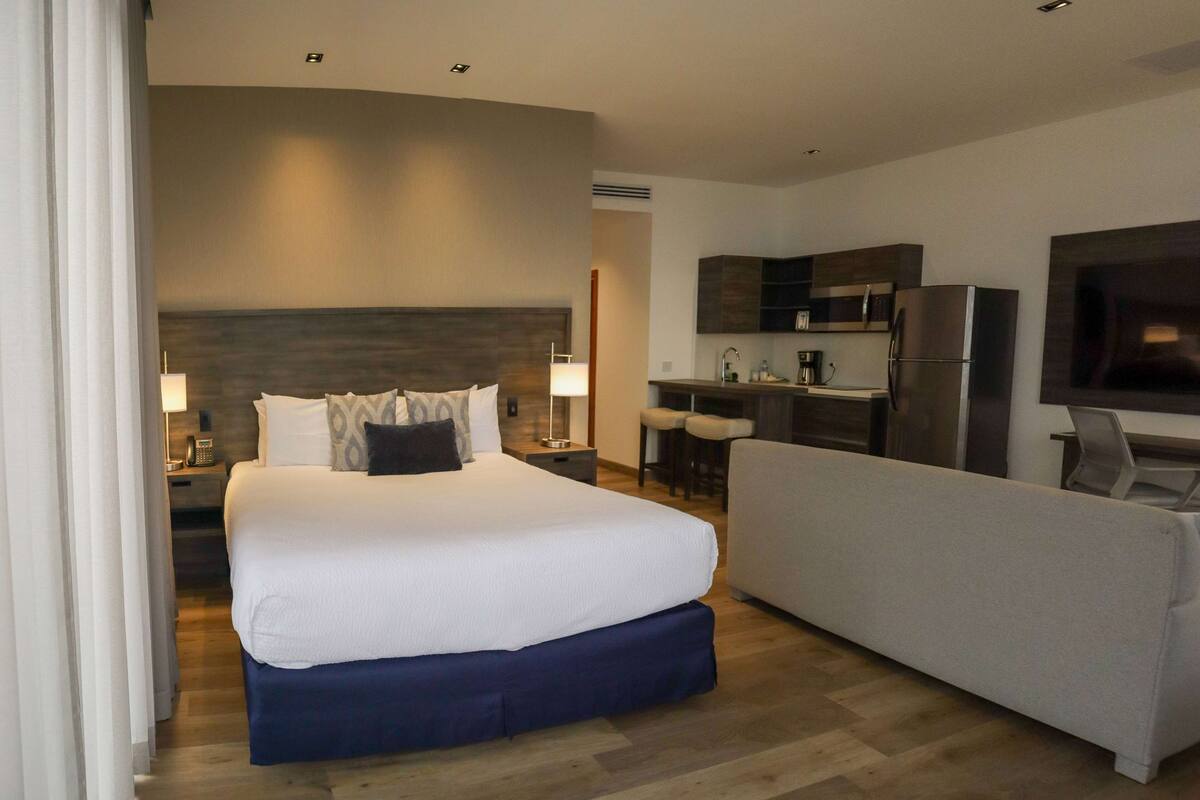 Ein Hotelzimmer mit einem großen Bett, einer Sitzecke, einer Küchenzeile und einem Flachbildfernseher.